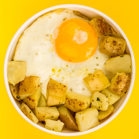 Fried Egg With Fried Potatoes Breakfast In A Bowl Against A Yellow Backgroundの写真素材