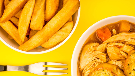 Traditional Chicken And Dumpling Casserole Against A Yellow Background With A Bowl Of Chips Or Friesの写真素材