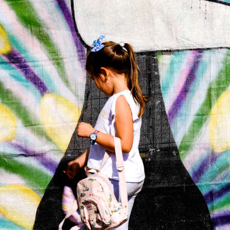 Young Girl Walking Past A Colourful Printed Background Screen Carrying A Backpackのeditorial素材
