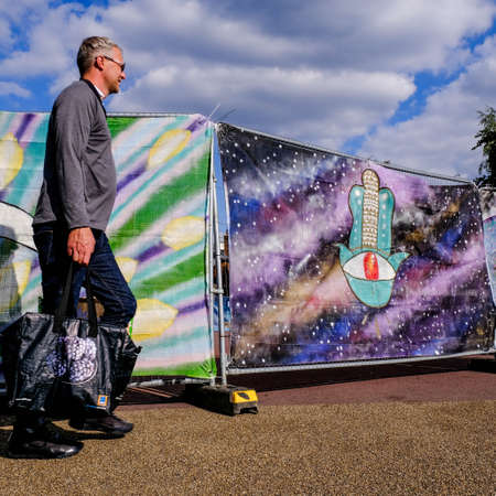 Anonymous Man Walking In Front Of A Painted Colourful Cloth Screen, Carring A Bag Of Shopping