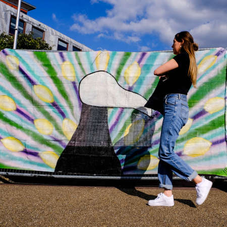 Young Anonymous Woman Walking In Front Of A Colourful Painted Cloth Screen Outside