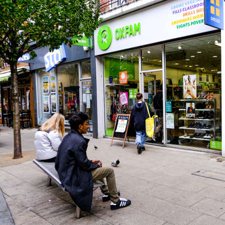 High Street Oxfam Charity Shop Outlet With people Seated Outside On A Bench