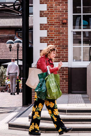 Epsom Surrey, London UK, June 10 2022, Woman Carrying Shopping Bags Wearing Colourul Floral Trousers Walking Aloneのeditorial素材