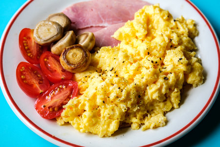 London UK June 25 2025, Scrambled Eggs With Fresh Tomatoes Fried Mushrooms and Slices Of Cooked Hamの写真素材