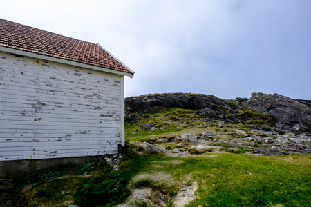 Olberg; Olbergstranden; Raege; Norway; May 20 2023, Old Weathered Traditional Building With A Rocky Outcrop Landscape In The Background Under A Misty Blue Skyの写真素材
