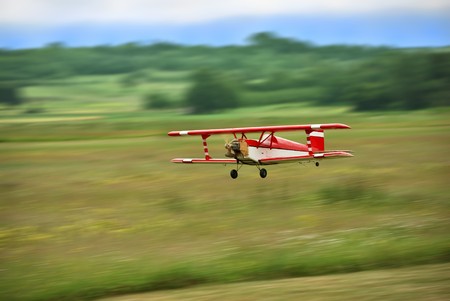 Red and white radio controlled aircraft with methanol engine flying over grassy field. The image...
