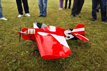 Red and white radio controlled aircraft with methanol engine on a grassy field.の写真素材