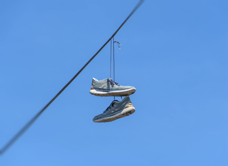 Shoes dangling on a cable over the street have many explanations, from celebrating one's birthday or wedding and making fun of drunk friends, to marking a location of drug dealers and bullying.の写真素材