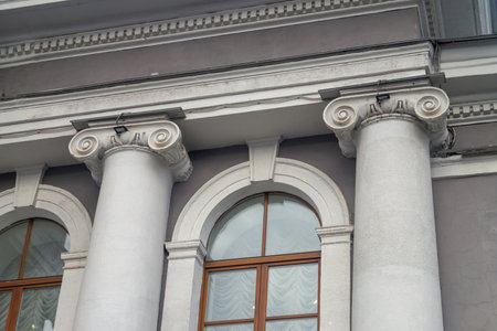 Facade fragment of an old classicism style building with Ionic columns and an arched window. Architectural background symbolizing justice, government, education, or culture and financeの写真素材