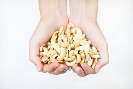 beautiful hands holding fresh roasted cashew nuts on white backgroundの写真素材