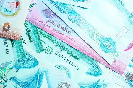 A high-quality, top-down view of United Arab Emirates currency (AED), featuring a mix of colorful Emirati banknotes and silver Dirham coins. The image showcases the detailed design of the UAE Dirham, including local cultural symbols and the portrait of Sheikh Zayed. This professional shot represents wealth, the Middle Eastern economy, and financial growth in Dubai and Abu Dhabi. Perfect for use in banking, investment, travel, and global finance-related content.の写真素材