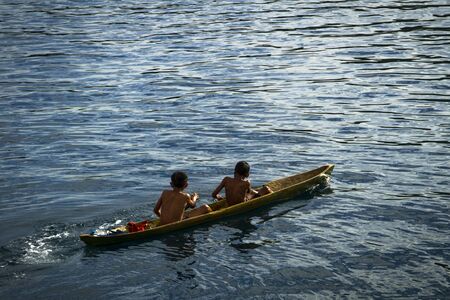 Local fisherman young boys play on the small traditional paddle boatの写真素材