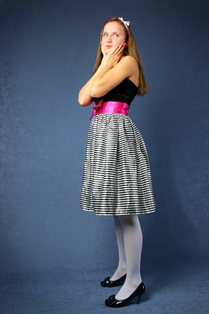 Young cute woman in bright dress with hands on face stands over blue backgroundの写真素材