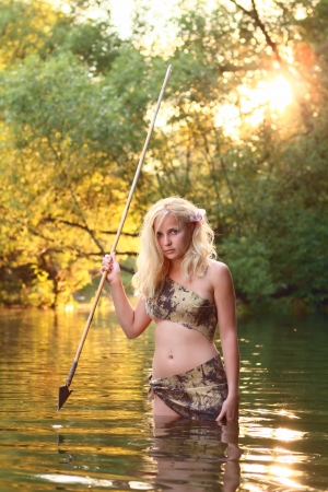 cute savage girl with gaff stands in the water of riverの写真素材
