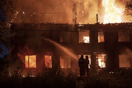 two firefighters extinguish burning house in the darkの写真素材