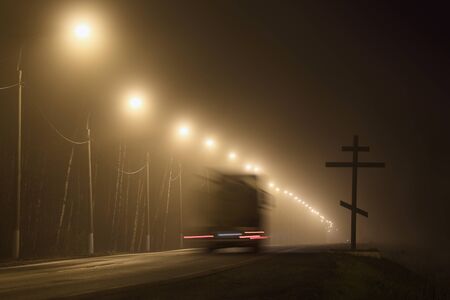 motion blurred truck moves on the road past the christian cross at night in the heavy fogの写真素材