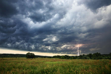stormy weather - dark clouds wih lightning above green field of grassの写真素材