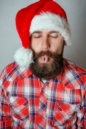 Portrait of a cool handsome brutal man in Christmas hat showing his tongue. Over red background. Rock musician.の写真素材