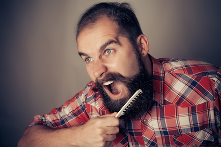 young man comb his beard and moustache on gray backgroundの写真素材