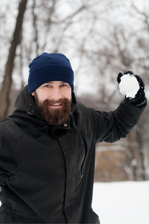 Portrait of a smiling young man in an ear flap hat with a snowball in his handの写真素材