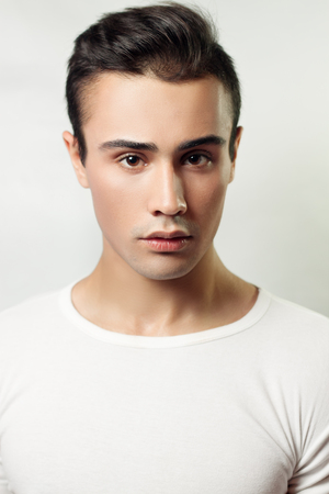 Handsome young man portrait. brunette guy in white t-shirt on a light background Used, clean skin, studio shot, beautyの写真素材