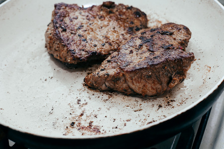 juicy beef steaks in the frying pan, two pieces of fried until golden brown, white panの写真素材