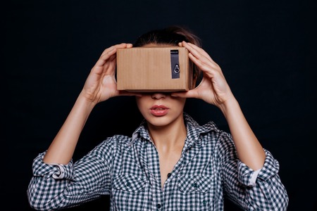 Color shot of a young woman looking through a cardboard, a device with which one can experience virtual reality on a mobile phone.の写真素材