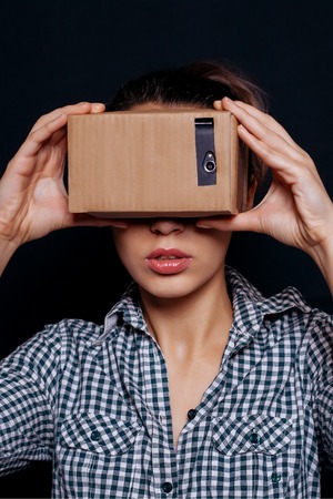 Color shot of a young woman looking through a cardboard, a device with which one can experience virtual reality on a mobile phone.の写真素材
