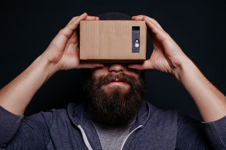 Color shot of a young woman looking through a cardboard, a device with which one can experience virtual reality on a mobile phone.の写真素材