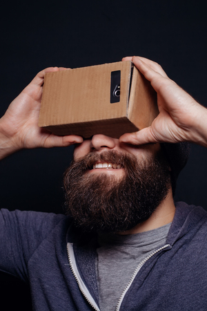 Color shot of a young man looking through a card board, a device with which one can experience virtual reality on a mobile phone. guy smilingの写真素材