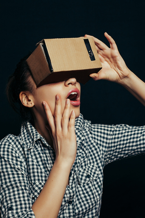 Color shot of a young woman looking through a cardboard, a device with which one can experience virtual reality on a mobile phone.の写真素材