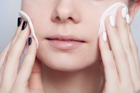 Woman using cotton pad. Happy smiling beautiful young woman cleaning skin by cotton pad. light background.の写真素材