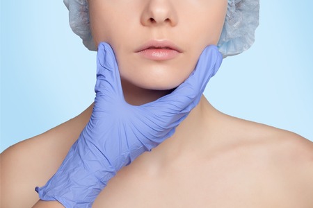 Botox injection. Attractive young woman in medical headwear and sketches on face keeping eyes closed while doctors hand making an injection in faceの写真素材