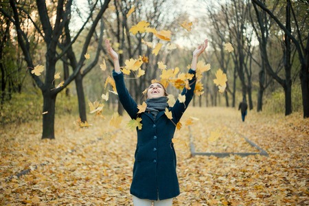 Woman throwing yellow leaves in the airの写真素材