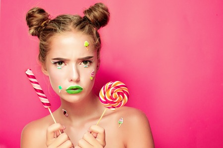 Beautiful young woman holds in hands candy smiling broadly. Stylish girl with bright makeup and candy in her hands, isolated on pink backgroundの写真素材