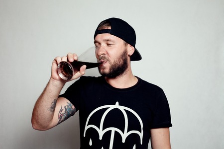 Drunk tattooed bearded man in a blak T-shirt isolated on a grey background. A guy with a glassの写真素材