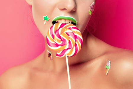 Beautiful young woman holds in hands candy smiling broadly. Stylish girl with bright makeup and...