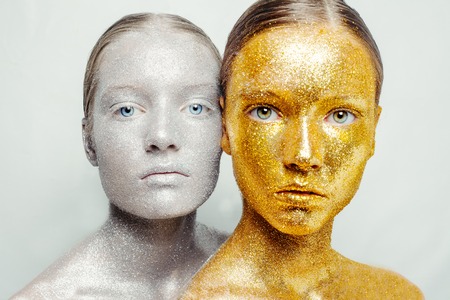 Beautiful, amazing portrait of two woman. Unreal make up like a space. Closeup shooting in studio with silver background. Emotion, posing of model. gold silver glitter.の写真素材