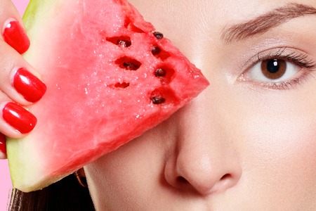 Beautiful young sexy woman girl in straight brunette hair long joyfully closes the eyes of watermelon and colorful swimsuit pretty smiles has blue eyes on a white pink background.の写真素材