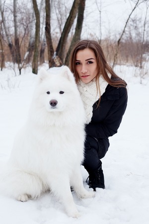 winter, christmas, animal, people, beauty concept- happy young woman owner petting embracing white Samoyed dog on snowの写真素材