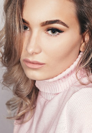 people, beauty, lifestyle, fashion and sensitive concept - Closeup sensual portrait of beautiful girl in the studio. girl in a pink sweater, hands near the face, eyes closedの写真素材