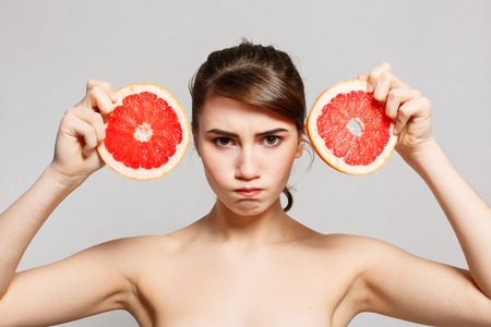emotions, health, people, food and beauty concept -Beauty portrait of a happy woman holding a grapefruit, emotional portrait. girl is angryの写真素材