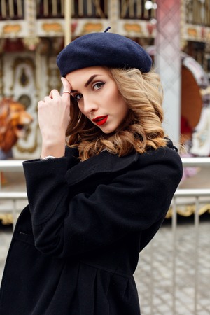 emotions, people, beauty and lifestyle concept - Girl Frenchwoman, against a merry-go-round. Street photo of young woman wearing stylish classic clothes. Female fashion concept. French style.の写真素材