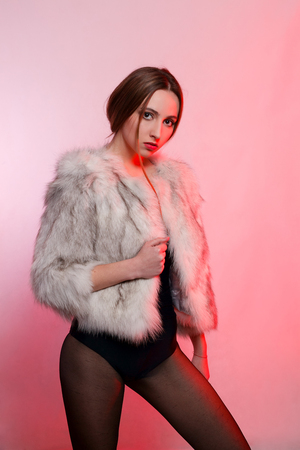 emotions, people, beauty, fashion and lifestyle concept - Fashionable beautiful woman in a gray fur coat of artificial fur on a red background stands frowningの写真素材