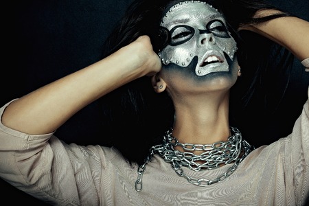 Halloween, holidays, lifestyle, people, beauty, creative concept- Halloween and creative make-up theme: beautiful girl model with black body with silver mask skull paint on dark background in studioの写真素材
