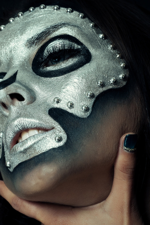 Halloween, holidays, lifestyle, people, beauty, creative concept- Halloween and creative make-up theme: beautiful girl model with black body with silver mask skull paint on dark background in studioの写真素材