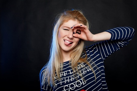 Charming young girl with a slender figure in elegant black dress shows the sign of OKの写真素材