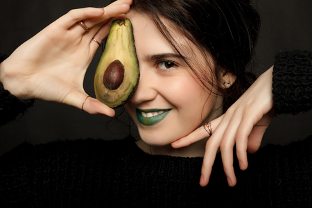 emotions, health, people, food and beauty concept - portrait of attractive caucasian smiling woman isolated on black studio shot with avocadoの写真素材