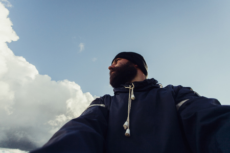 tourism, mountains, lifestyle, nature, people, Selfie concept - Young Man Traveler Makes Selfie On Background Mountains In Summer, at sunset. bearded tourist smilingの写真素材
