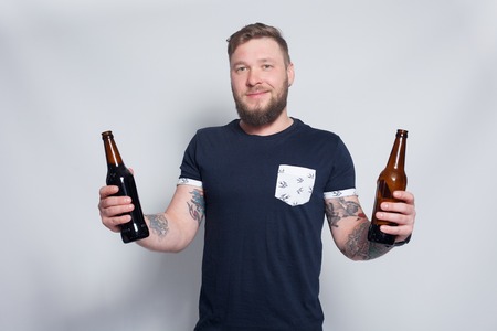 people, 4K and lifestyle concept - Brutal bearded male with tattooed arm drinks a beer from a bottle. handsome man in hat.Brutal bearded boy with tattooの写真素材